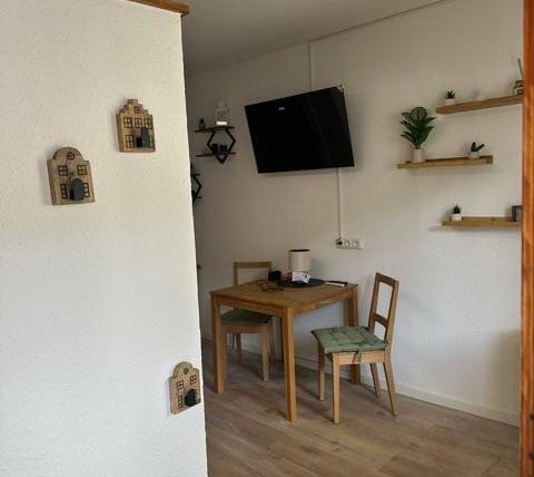 Un espace de vie confortable avec une table à manger et des chaises. Sur le mur, il y a des étagères avec des plantes et des décorations.
