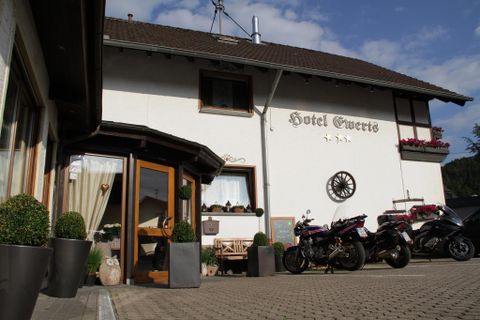 Ein gemütliches Hotel mit dem Namen "Hotel Gewerts". Vor dem Gebäude stehen Motorräder und es gibt grüne Pflanzen in Töpfen.