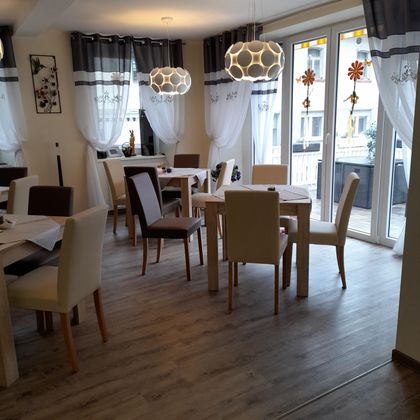 A bright restaurant with wooden floors and modern furniture. Large windows with curtains let in plenty of light.