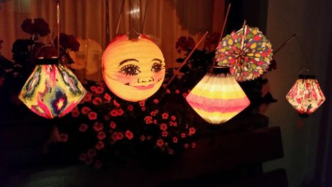 Bunte Laternen in verschiedenen Formen hängen an einer Wand. Sie strahlen ein warmes Licht und verleihen der Umgebung eine festliche Atmosphäre.