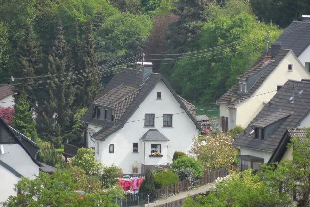 Un quartier résidentiel calme avec un appartement blanc entouré d'arbres. Certaines maisons ont des jardins et les environs sont verts et accueillants.