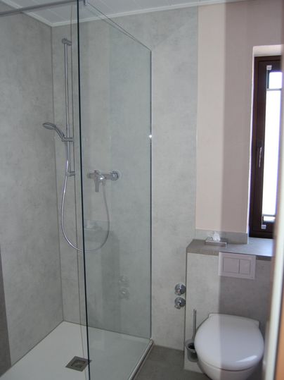 Een modern badkamer met een glazen douche. De muren zijn in neutrale grijstinten gehouden, en een raam zorgt voor natuurlijk licht.