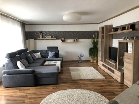 Een moderne woonkamer met een grijze bank en houten meubels. De ruimte is licht en gezellig ingericht.