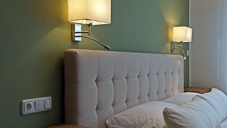 Une chambre moderne avec une tête de lit capitonnée et des coussins confortables. Une lumière chaude des lampes murales crée une atmosphère accueillante.