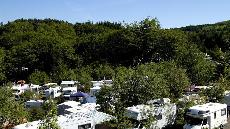 A campsite with many motorhomes amidst trees. The green surroundings create a peaceful atmosphere.