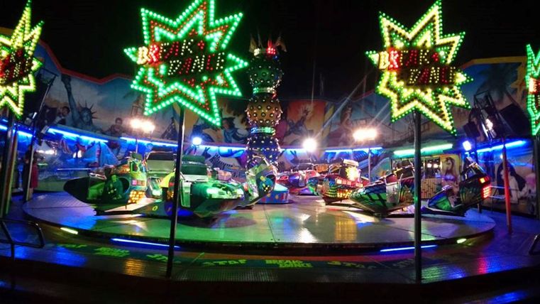 Ein bunter Jahrmarkt mit einem Karussell voller Lichter. Die leuchtenden Sterne und bunten Fahrzeuge schaffen eine fröhliche Atmosphäre.