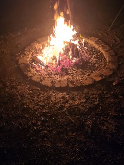 Ein Lagerfeuer in einem Steinkreis leuchtet hell in der Dunkelheit. Rauch steigt in die Nacht auf und es ist eine gemütliche Atmosphäre zu spüren.