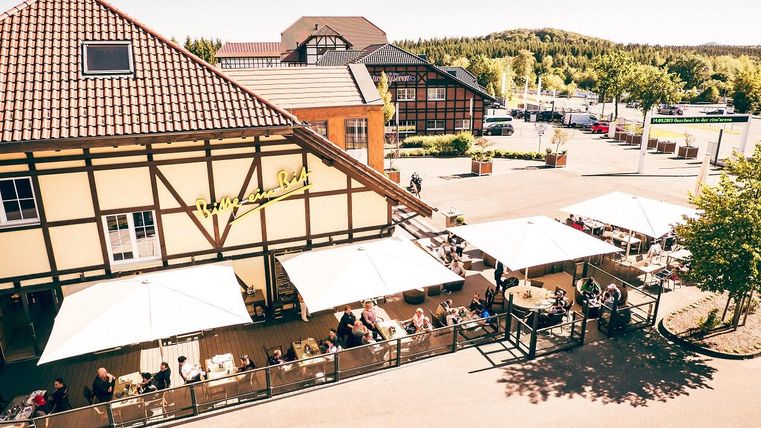 Un restaurant sous un lumineux soleil avec de grands parasols. Beaucoup de clients sont assis à l'extérieur et profitent de l'atmosphère.
