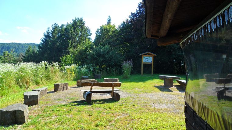 A quiet place in nature with a meadow and benches made of wood. In the background, trees and an information sign are visible.