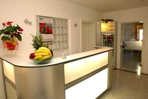 Eine helle Empfangstheke mit einer Obstschale und einer Pflanze. Im Hintergrund befindet sich ein Kühlschrank und ein Zugang zu einem weiteren Raum.