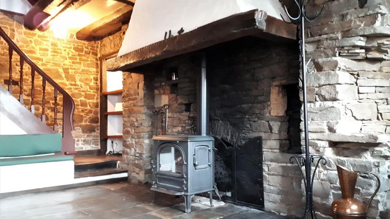 A cozy room with a stone fireplace and modern heating. The walls are made of natural stone and there is a staircase in the background.