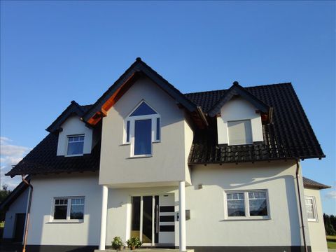 A modern house with a sloping roof and large windows. The sky is clear and blue.