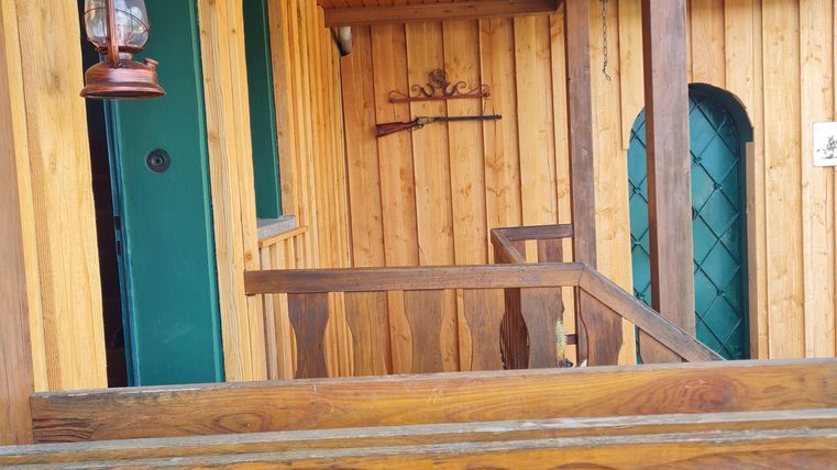 Een gezellige houten veranda met een groene deurkozijn. Aan de muur hangt een lantaarn en er zijn decoratieve elementen op de houten plank.