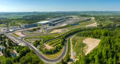 Eine große Rennstrecke umgeben von grünen Hügeln. Im Hintergrund sind die Tribünen und die Boxenanlage zu sehen.