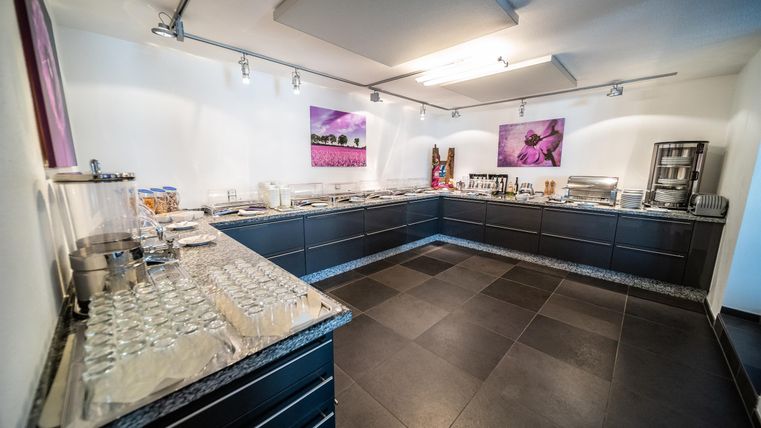 Een moderne ruimte met een elegante buffetbar en zwarte kasten. De muren zijn eenvoudig en licht, versierd met kleurrijke afbeeldingen.