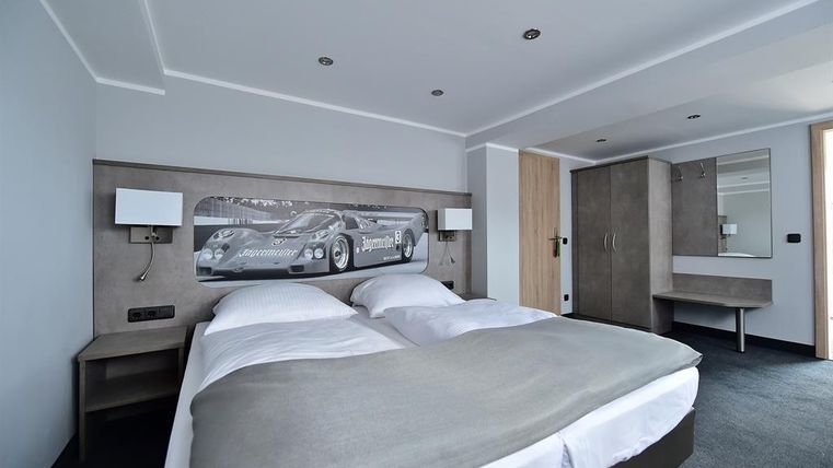 Ein modernes Schlafzimmer mit einem Doppelbett und einem großen Fenster. An der Wand hängt ein Bild eines Rennwagens.