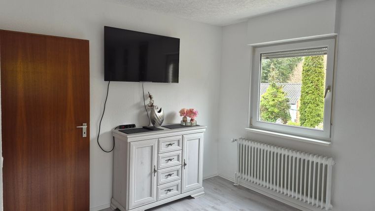 A bright room with a television on the wall and a white sideboard. The window offers a view of the green surroundings.