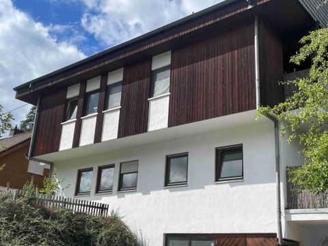 Ein modernes Haus mit einer Kombination aus Holz- und Putzfassade. Im untern Bereich liegt die Ferienwohnung. Der Himmel ist teilweise bewölkt und die Umgebung ist grün.
