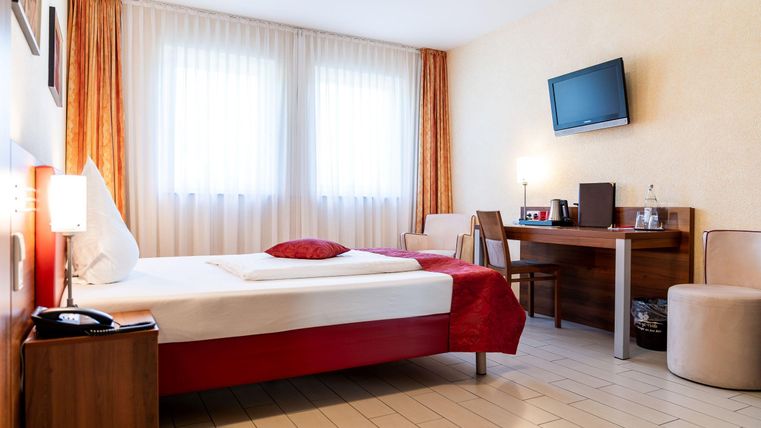 Een gezellig hotelkamertje met een groot bed, een bureau en een televisie. De grote ramen zorgen voor veel daglicht.