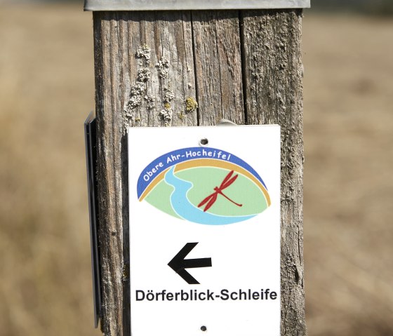 Holzpfosten mit Schild zur Dörferblick-Schleife in der Oberen Ahr-Hocheifel. Pfeil zeigt nach links. Hintergrund unscharf., © Tourist-Information Hocheifel-Nürburgring©JonathanAndrews