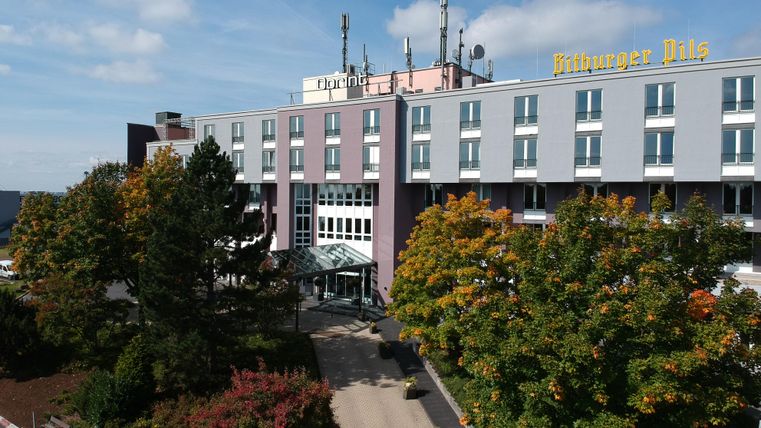 A modern hotel building with a clear sky and colorful trees. The entrance is inviting and the facade is in soft colors.