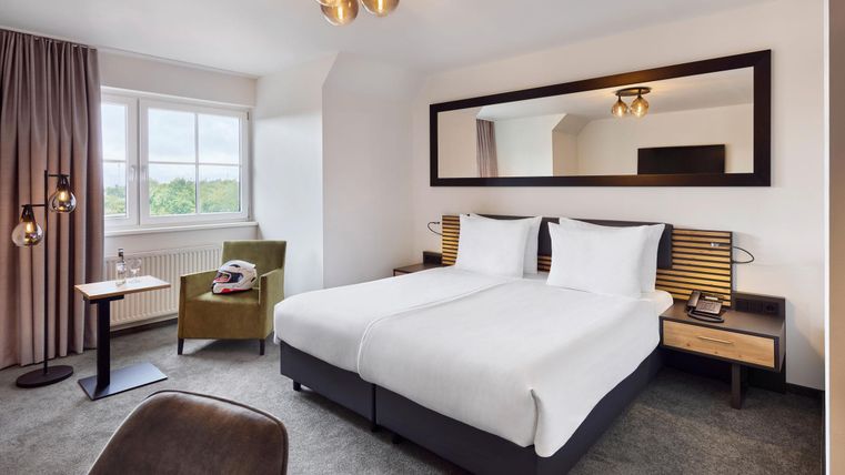 Een moderne hotelkamer met twee eenpersoonsbedden en een grote spiegel. De kamer is licht en stijlvol ingericht, met een gezellige stoel en mooie decoratieve elementen.