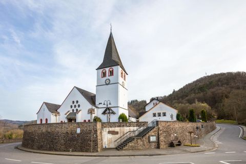 Een kerk met een markante toren en witte muren, omgeven door een stenen muur. Op de achtergrond strekken zich zachte heuvels uit.