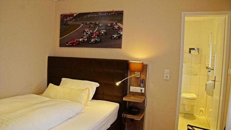 Une chambre confortable avec un lit simple et une image de télévision d'une course automobile. En arrière-plan, une petite salle de bain est visible.