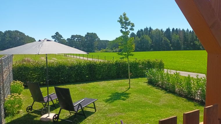 Een rustige tuin met twee ligstoelen en een parasol. Op de achtergrond zijn groene velden en bomen te zien.
