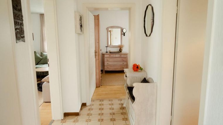 Ein heller Flur mit einem hübschen Bodenmuster. An der Wand hängen Bilder und am Ende des Flurs steht ein Spiegel mit einem Tisch.