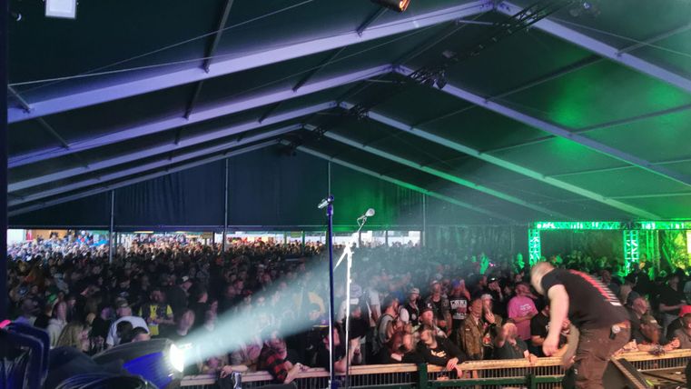 A large crowd in a tent at a concert. In the foreground, a musician can be seen playing on stage.