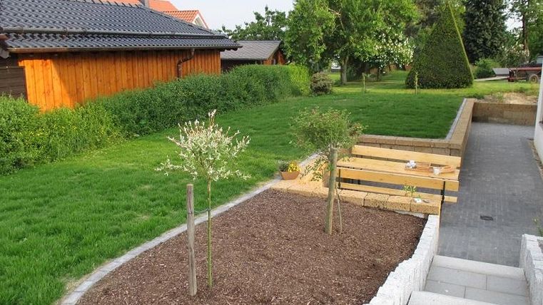 Un beau jardin avec une pelouse et des arbres. À l'arrière-plan, on peut voir des cabanes en bois et une terrasse.