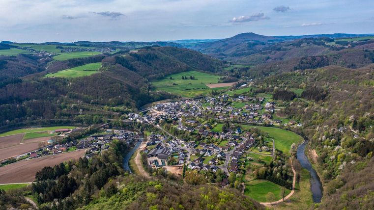 Eine malerische Aussicht auf ein kleines Dorf in einer hügeligen Landschaft. Umgeben von grünen Feldern und einem fließenden Fluss.