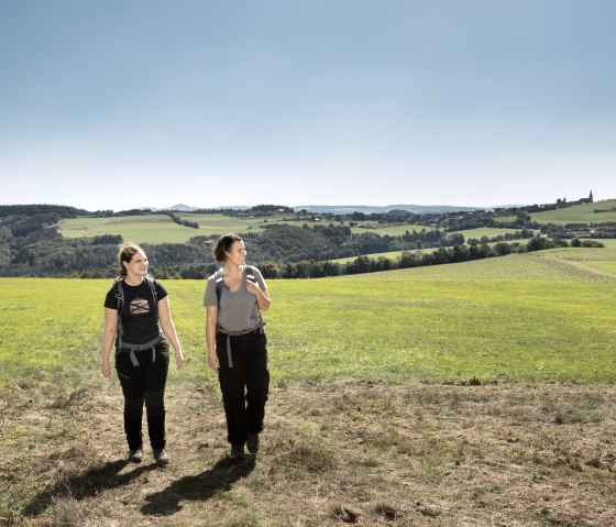 Two women are walking along a country lane through a green landscape with hills and a clear blue sky in the background., &copy; TI Hocheifel-N&uuml;rburgirng&copy;BaumannFotografie