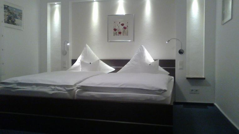 Een moderne slaapkamer met een tweepersoonsbed en elegante kussens. De muren zijn licht en goed verlicht, versierd met afbeeldingen.