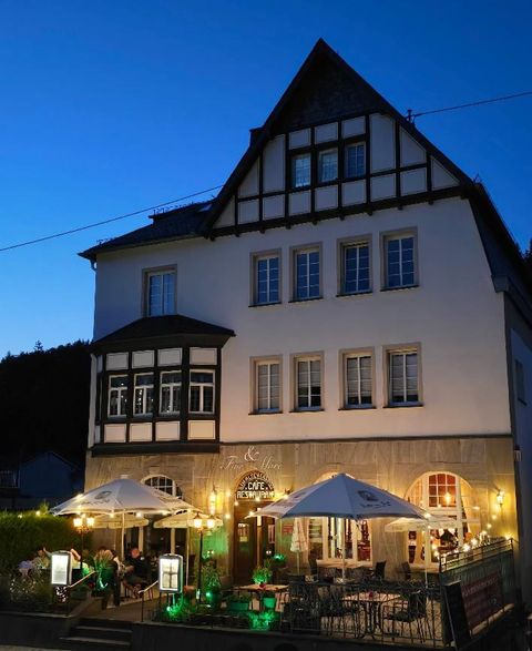 Un bâtiment charmant avec une architecture traditionnelle au crépuscule. Les tables en extérieur sont décorées de lumières, et l'atmosphère est accueillante.