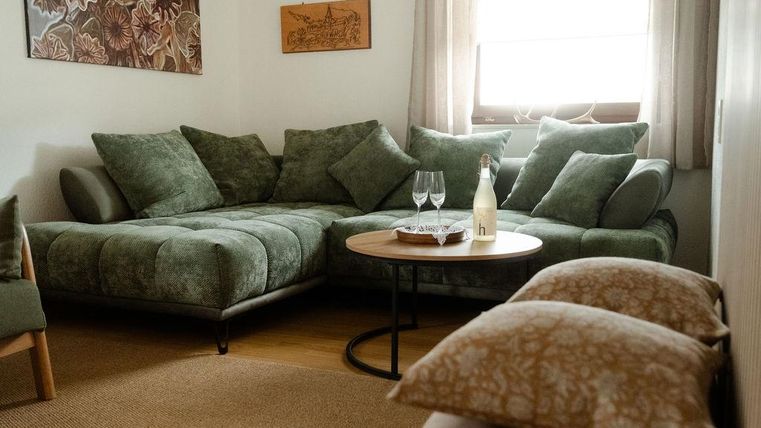 Ein gemütliches Wohnzimmer mit einem grünen Sofa und einer runden Tisch. Auf dem Tisch stehen zwei Gläser und eine Flasche.