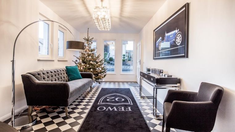 Ein eleganter Eingangsbereich mit einem grauen Sofa und einem modernen Sessel. Ein Weihnachtsbaum steht in der Ecke, und die Wände sind hell mit einem ansprechenden Bodenbelag.