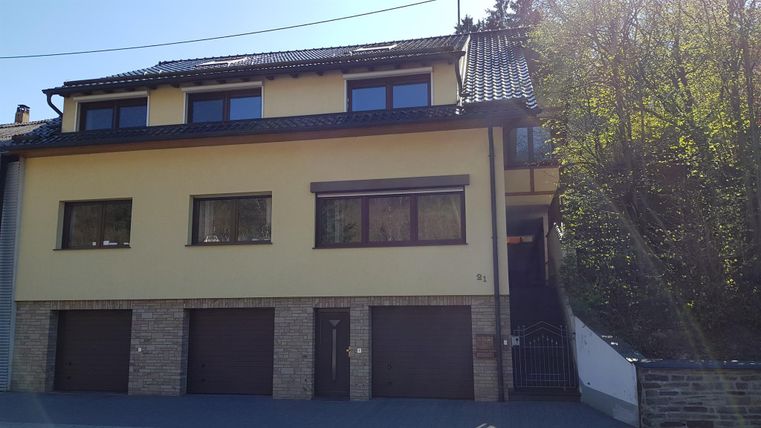 Een modern huis met een gele gevel en twee garages. Het bevindt zich in een rustige, natuurlijke omgeving.