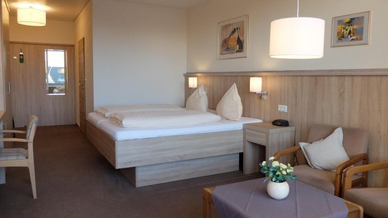 Een gezellige kamer met twee bedden, houten decor en zachte verlichting. Er is een tafel en stoelen, evenals decoratieve elementen aan de muren.