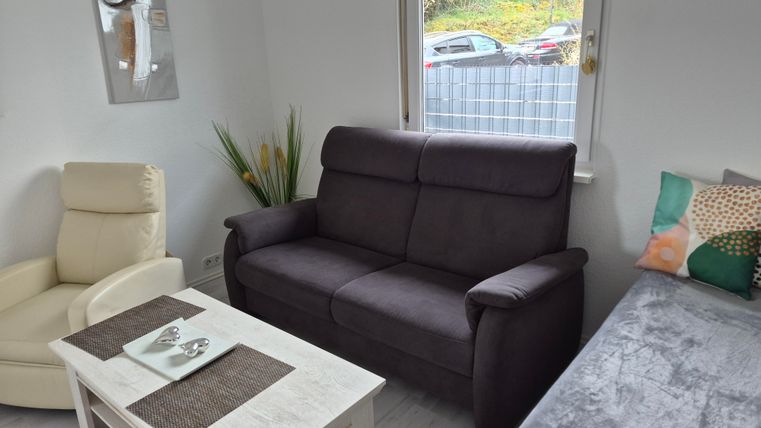 A cozy living room with a dark gray sofa and a light armchair. The table is covered with a tablecloth and decorations, and the window offers a view outside.