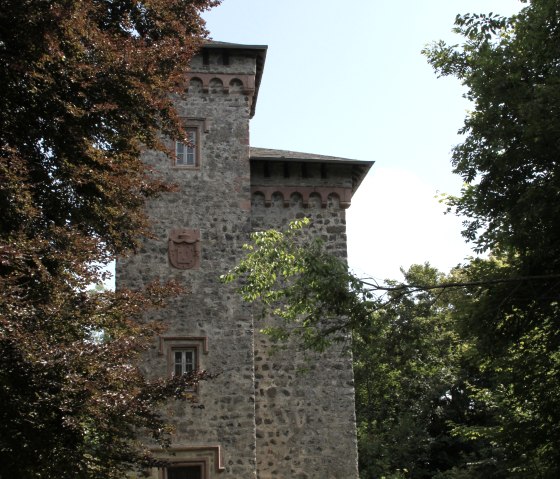 Ein  Steinturm mit Zinnen steht inmitten von B&auml;umen und einer gr&uuml;nen Wiese. Der Himmel ist klar und blau., &copy; Eifel Tourismus GmbH