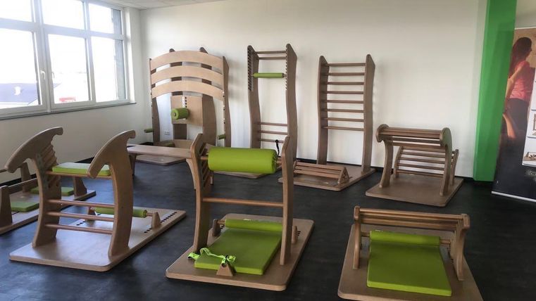 A modern gym with various training equipment made of wood and green upholstery. The equipment is functionally arranged and provides a bright, inviting atmosphere.