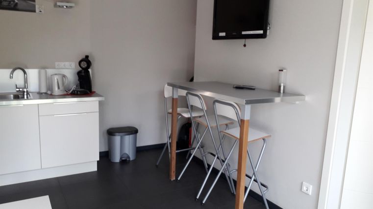 Eine moderne Küche mit einem kleinen Tisch und Stühlen. An der Wand hängt ein Fernseher und eine Uhr.