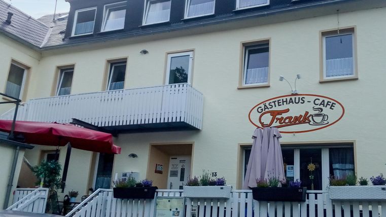 A cozy guesthouse with a café. The facade is painted in light colors and decorated with flowers.