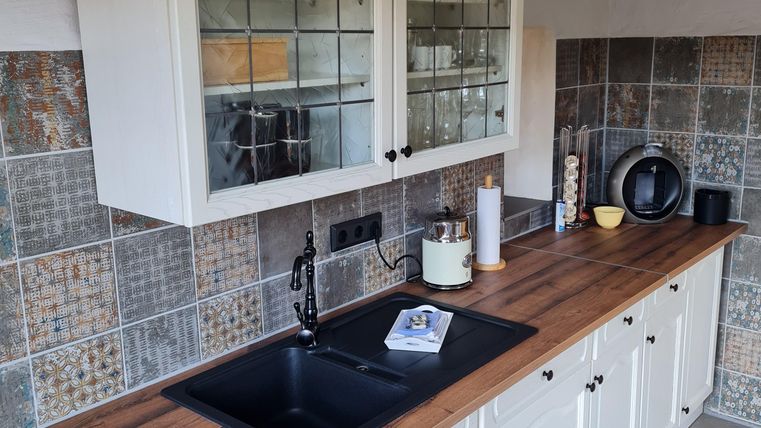 Een moderne keuken met een houten werkblad en witte kasten. De muren zijn versierd met tegelachtige patronen.