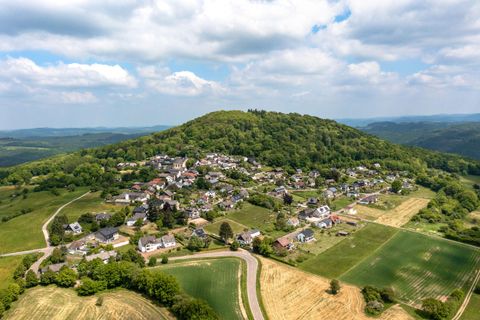 Een luchtfoto van een klein dorp, omringd door groene heuvels en velden. De lucht is bewolkt en het landschap is schilderachtig en vredig.