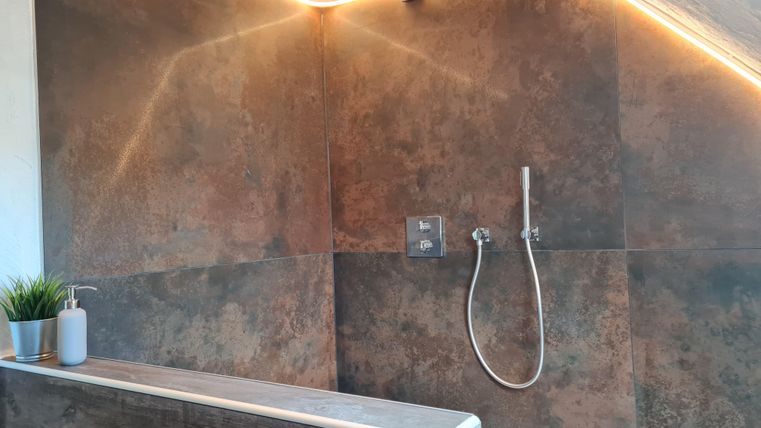 Een modern ingericht badkamer met een douche en zachte verlichting. De wanden zijn in een warme, metallic tint gehouden.