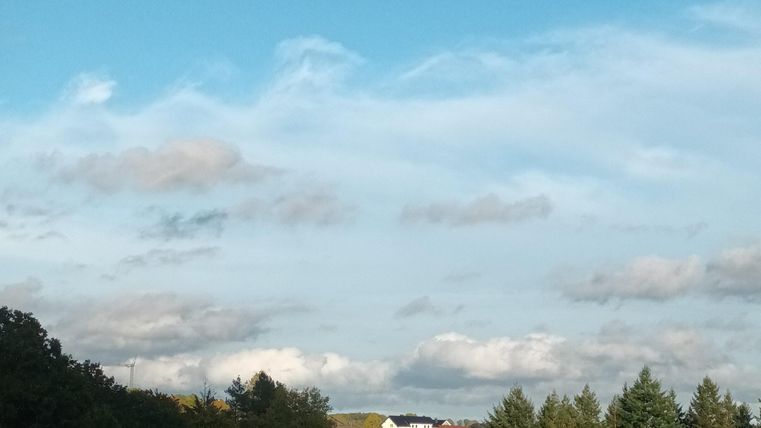 Een rustige landschap met groene bomen en een blauwe lucht. Op de achtergrond zijn wolken te zien.