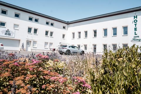 Een modern hotelgebouw met een mooie tuin en kleurrijke bloemen. Op de voorgrond is een parkeerplaats met een auto zichtbaar.